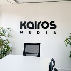 Modern office wall with Kairos Media logo above desk and chair.